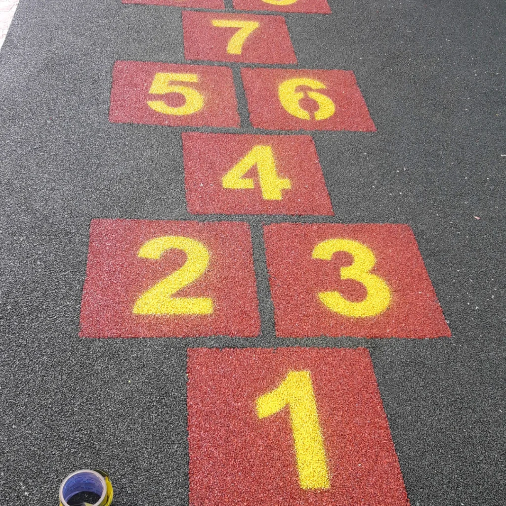 Playground com Paginação de Jogo Amarelinha com Blocos na cor Terracota e Números na cor Amarela no chão Preto.
