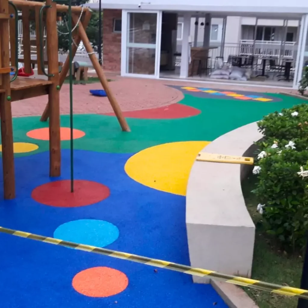Um parque infantil na cor Amarela, Azul, Rosa Salmão com um escorregador, balanços e uma estrutura de brincar.