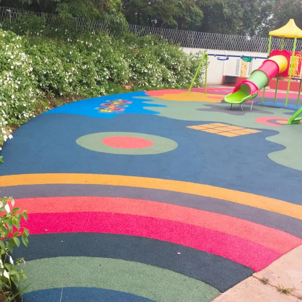 Um parque infantil com piso contínuo na paginação de cores Amarela, Azul, Rosa Salmão com um escorregador, balanços e uma estrutura de brincar.